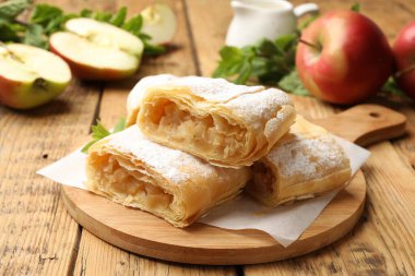 Lezzetli elmalı turta parçaları pudra şekeri ve ahşap masada meyveler, yakın plan.