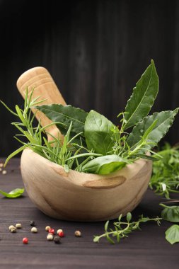 Farklı taze bitkilerle havan topu, biber ve ahşap masa üzerinde koyu arkaplan, yakın plan