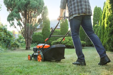 Bahçede çim biçme makinesiyle çimen biçen adam, yakın plan.