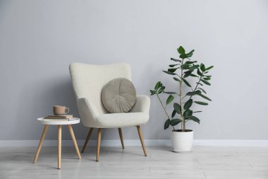 Açık gri duvarın yanında rahat bir koltuk ve dekor.