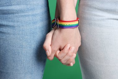 LGBT konsepti. Gökkuşağı bileklikli kadınlar yeşil arka planda el ele tutuşuyorlar, yakın plan.