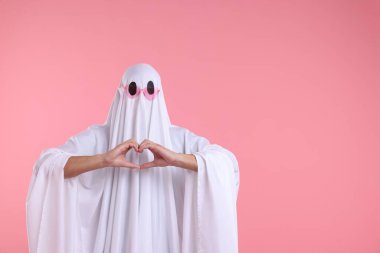 Şirin hayalet. Güneş gözlüklü beyaz çarşaflı bir adam pembe arka planda kalp hareketi yapıyor.