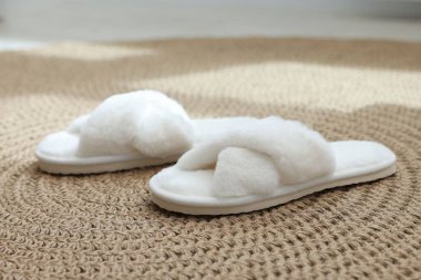 Hasır üzerinde tüylü beyaz terlikler, yakın plan.