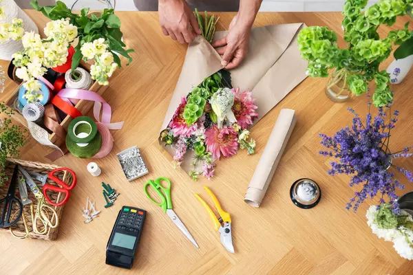 Ahşap masada çiçek buketi yapan profesyonel bir çiçekçi.