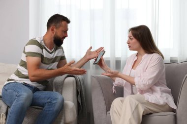 İhanet. Karısı evdeki kanepede sadakatsiz kocasına kanıtlarla akıllı telefon gösteriyor.