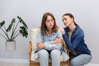 Gri duvarın yanındaki koltukta oturan, gücenmiş arkadaşından özür dileyen kadın.