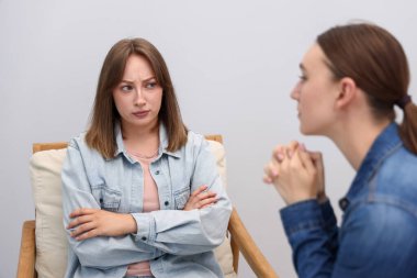 Gri duvarın yanındaki koltukta oturan, gücenmiş arkadaşından özür dileyen kadın.