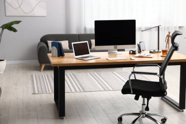 Modern bilgisayarı, diğer cihazları ve ahşap masa üzerindeki kırtasiyesi olan şık bir iş yeri.