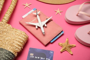Uçak modeli, pasaport, uçuş bileti, kredi kartı ve pembe arka planda plaj aksesuarları.