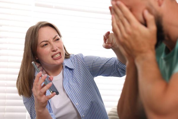 Предательство. Эмоциональная жена показывает смартфон с доказательствами своему неверному мужу дома, избирательный фокус