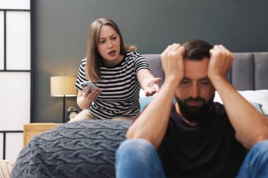 İhanet. Akıllı telefonlu kızgın bir kadın evde yatağında rahatsız kocasına bağırıyor, seçici bir şekilde.