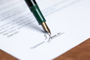 Kahverengi masadaki dolma kalemle noter belgesi imzalanırken, yakın plan