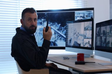 Güvenlik görevlisi güvenlik kameralarını izliyor ve ofiste telsiz kullanıyor.