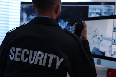 Güvenlik görevlisi mobese kameralarını izliyor ve ofiste telsiz kullanıyor.