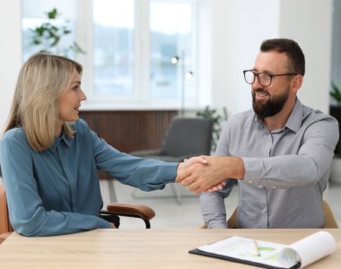 Gülümseyen iş ortakları ofiste el sıkışıyor.