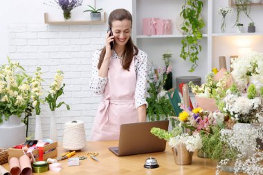 Profesyonel çiçekçi dükkanda çalışırken akıllı telefondan konuşuyor.