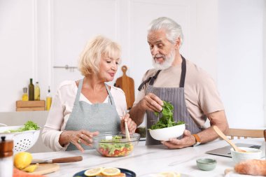 Yaşlı çift mutfaktaki masada birlikte yemek pişiriyor.