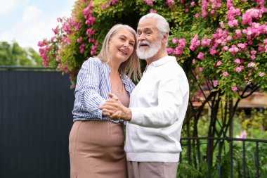Güzel yaşlı çift, açık havada pembe güllerin arasında dans ediyor.