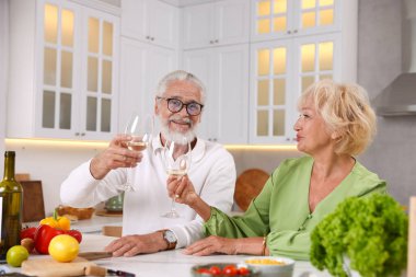 Yaşlı çift mutfakta yemek pişirirken beyaz şarap içiyor.