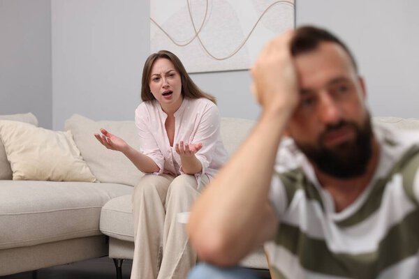 Предательство. Злая женщина кричит на своего оскорбленного мужа на диване дома, избирательный фокус