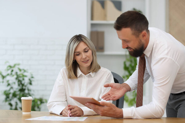 Smiling business partners working with tablet at table in office