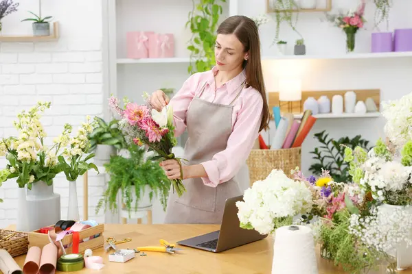 Profesyonel çiçekçi dükkandaki ahşap masada çiçek buketi yapıyor.