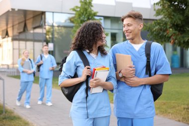 Sırt çantalı ve defterli tıp öğrencileri açık havada, seçici bir odak noktası.