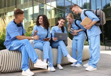 Üniformalı bir grup tıp öğrencisi açık hava binasının yakınında birlikte okuyorlar.