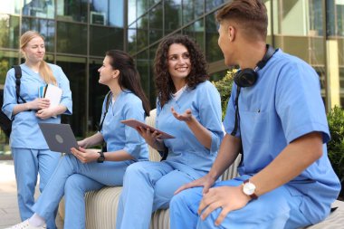 Üniformalı bir grup tıp öğrencisi açık hava binasının yakınında birlikte okuyorlar.