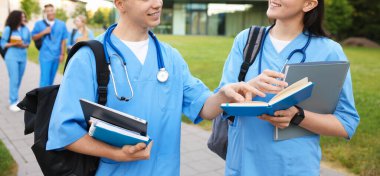 Sırt çantalı ve defterli tıp öğrencileri açık havada, seçici bir odak noktası.