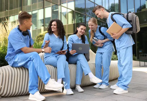 Üniformalı bir grup tıp öğrencisi açık hava binasının yakınında birlikte okuyorlar.