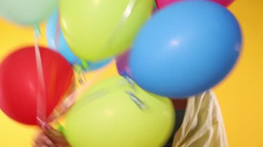 Sarı arka planda renkli balonları olan mutlu bir kadın.