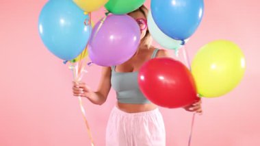 Gözlüklü, pembe arka planda renkli balonları olan gülümseyen kadın.