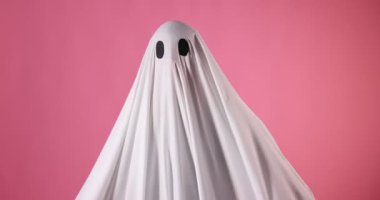 Ürkütücü hayalet. Pembe arka planda korkutucu hareketler gösteren beyaz çarşaflı bir adam.