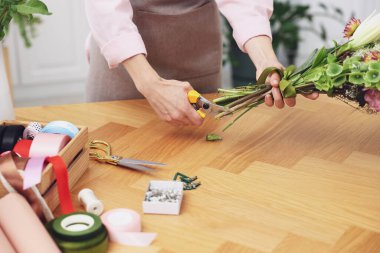 Dükkandaki ahşap masada çiçek buketi yapan profesyonel bir çiçekçi.