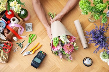 Ahşap masada çiçek buketi yapan profesyonel bir çiçekçi.