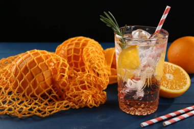 Bardakta portakallı maden suyu, mavi ahşap masada taze meyve ve pipetler, yakın plan.