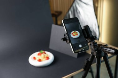 Stüdyoda akıllı telefonla lezzetli makarna çekmek, ekrana odaklanmak. Profesyonel yemek fotoğrafçılığı.