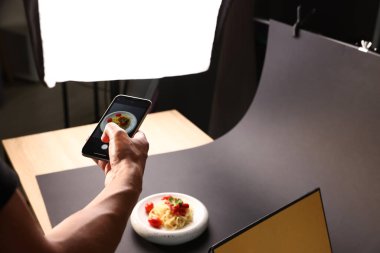 Adam stüdyoda akıllı telefonlu makarna fotoğrafı çekiyor, yakın plan. Profesyonel yemek fotoğrafçılığı.