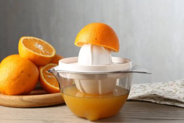 Meyve suyu. Meyve sıkacağı ve taze portakallar ahşap masada, yakın plan.