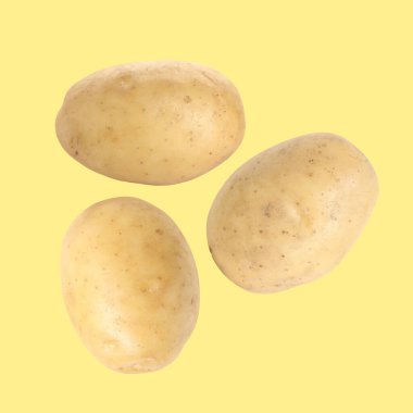 Soluk turuncu arka planda üç çiğ patates uçuşuyor.