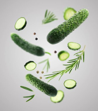 Taze salatalıklar, biberiye ve biber taneleri gri eğimli arka plana düşüyor.