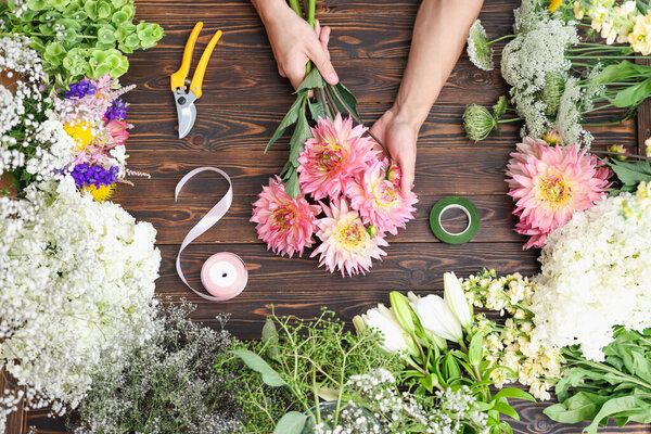 Профессиональный флорист делает букет цветов за деревянным столом, вид сверху
