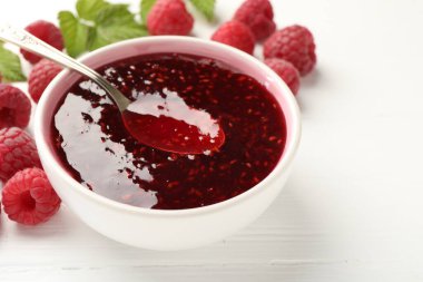 Tatlı ahududu reçeli kasede, böğürtlen ve yeşil yapraklar beyaz ahşap masada, yakın plan. Metin için boşluk