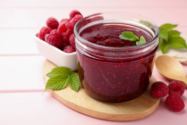 Cam kavanozda tatlı ahududu reçeli, pembe ahşap masada nane ve böğürtlen, yakın plan.