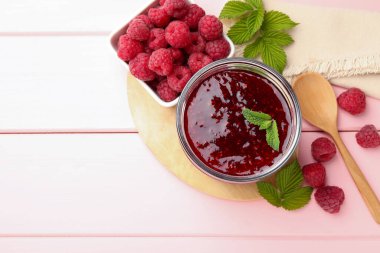 Cam kavanozda tatlı ahududu reçeli, pembe ahşap masada nane ve böğürtlen, düz yatak. Metin için boşluk