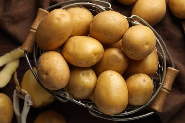 Kahverengi kumaş üzerinde bir sürü çiğ patates ve metal sepet vardı.