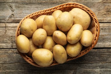 Hasır sepetin içinde bir sürü çiğ patates, ahşap masa, üst manzara.