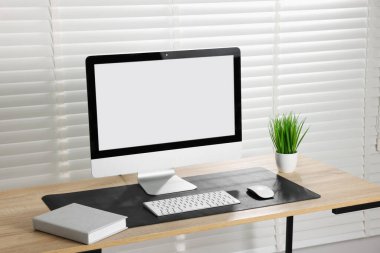 Kapalı alandaki ahşap masa üzerinde bilgisayar ve siyah fare altlığı olan şık bir iş yeri. Metin için boşluk