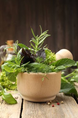 Farklı taze otlarla havan ve ahşap masa üzerinde biber, kahverengi arka plan, yakın çekim